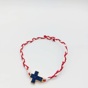 May include: A red and white braided bracelet with a blue glitter cross charm.