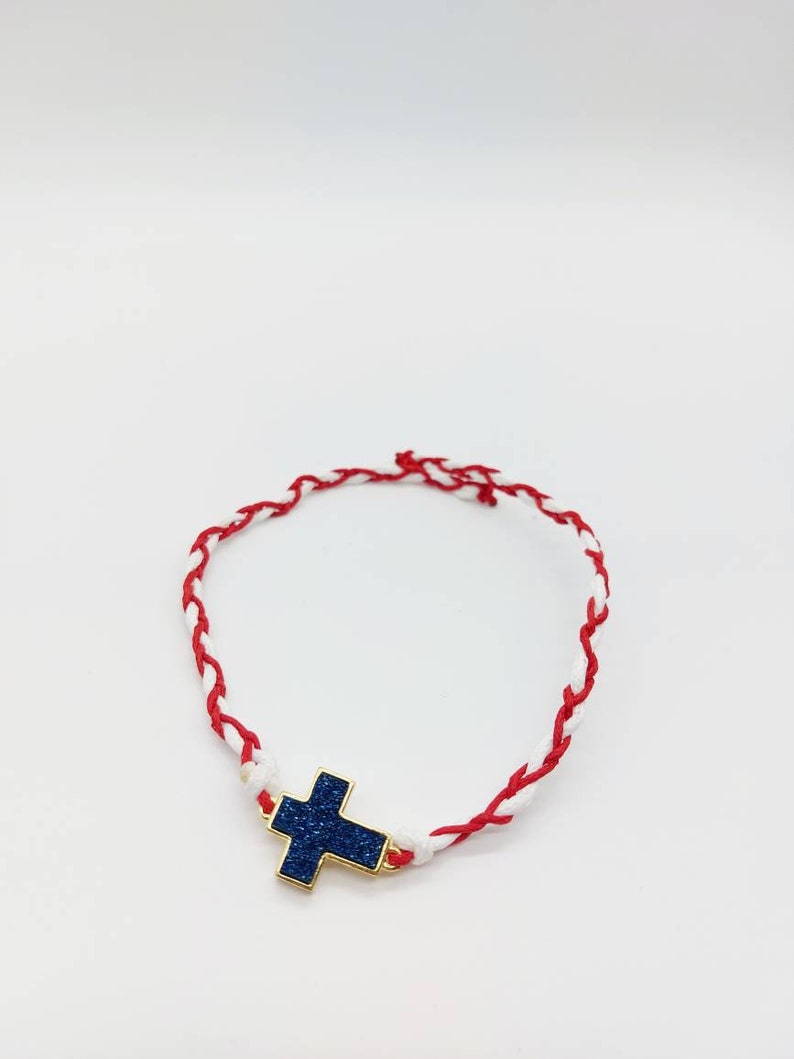 May include: A red and white braided bracelet with a blue glitter cross charm.