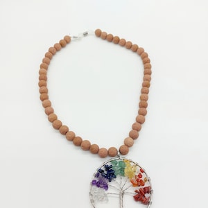 Puede incluir: Un collar de cuentas marrones con un colgante de plata en forma de árbol de la vida. El árbol está adornado con piedras preciosas de colores, que representan los siete chakras.