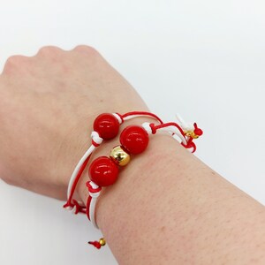 May include: Red and white string bracelet with three red beads and a gold bead.