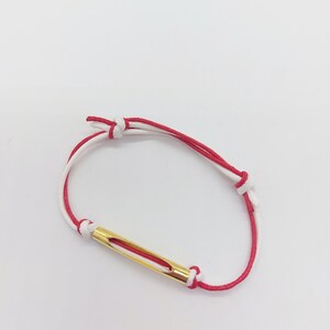 May include: A red and white string bracelet with a gold bar charm.