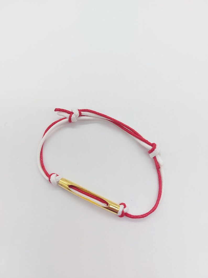 May include: A red and white string bracelet with a gold bar charm.