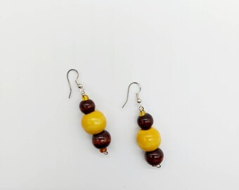 May include: A pair of wooden earrings with brown and yellow beads. The earrings are made of natural wood and have a simple, elegant design.