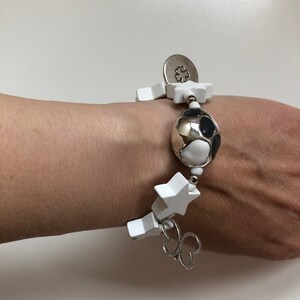 May include: White wooden star charm bracelet with a silver charm, a silver and black patterned bead, and a silver clover charm.