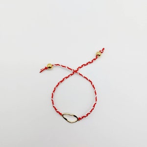 May include: A red and white string bracelet with a gold, irregular shaped charm.