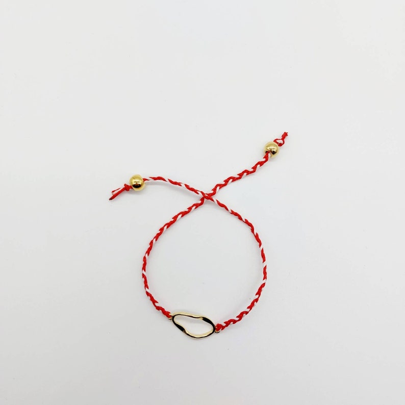 May include: A red and white string bracelet with a gold, irregular shaped charm.