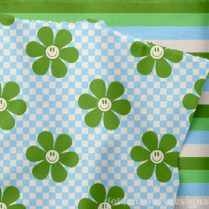 May include: A green and blue checkered fabric with a repeating pattern of green flowers with yellow smiley faces. The fabric is folded over itself, revealing the checkered pattern underneath.