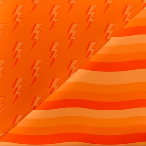 Puede incluir: Tela de color naranja y naranja claro con una costura diagonal. Un lado de la tela tiene un patrón repetido de rayos naranja. El otro lado de la tela tiene rayas horizontales.