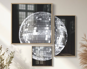 May include: Three framed black and white photographs of a disco ball hanging from the ceiling. The frames are wooden and have a light brown finish. The photographs are displayed on a white wall above a wooden bench with two beige ceramic vases.