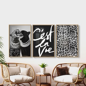May include: Three framed art prints. The left print shows two leopards wearing necklaces. The center print is black with white text that reads "C'est la Vie". The right print is a leopard print pattern.