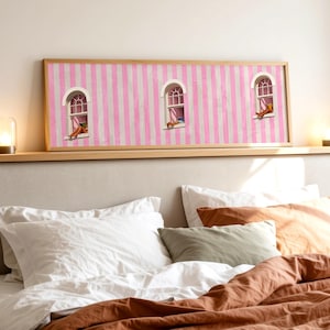 Puede incluir: Una pieza de arte mural rectangular en un marco de madera clara con un fondo de rayas verticales rosas y blancas. La obra muestra tres ventanas arqueadas, cada una con una pequeña figura sentada en el alféizar, en una paleta de colores suaves.
