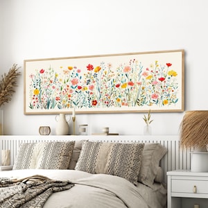 Puede incluir: Interior de dormitorio con una gran impresión floral enmarcada. La obra de arte presenta una variedad de coloridas flores silvestres. La cama está hecha con ropa de cama de tonos neutros y cojines estampados. También se ve una mesita de noche con una lámpara.
