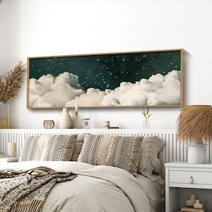 Puede incluir: Un dormitorio con una cama vestida con ropa de cama neutra, cojines estampados y una manta con flecos. Encima de la cama cuelga una obra de arte enmarcada que representa nubes y estrellas. La habitación está decorada en tonos neutros y texturas naturales.