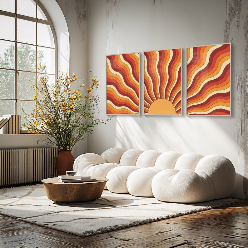 May include: Three abstract art prints with a retro sun design in shades of orange, red, and yellow. The prints are hung on a white wall above a white modular sofa.
