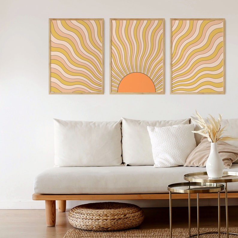 May include: Three framed prints with a retro sunburst design in shades of yellow, orange, and pink. The center print features a half-circle orange sun.