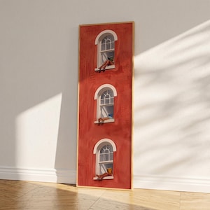 May include: A tall, rectangular framed wall art piece featuring a textured, deep red facade with three vertically aligned arched windows. Each window displays a figure sitting on the sill, with the top figure reading a book and the others resting.