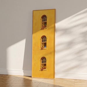 May include: A vertical artwork showing a yellow building facade with three arched windows. Each window depicts a person relaxing. The artwork is framed in a light wood colour and leans against a white wall and wooden floor.