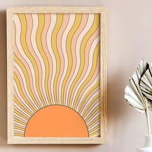 May include: A framed print of a retro sunburst design with a yellow, orange, and pink color scheme. The sunburst is made up of wavy lines that radiate outward from a central orange circle.