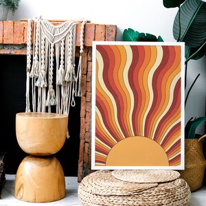 May include: A framed print with a retro sunburst design in shades of orange, red, and yellow. The print is hanging on a brick wall above a wooden stool.