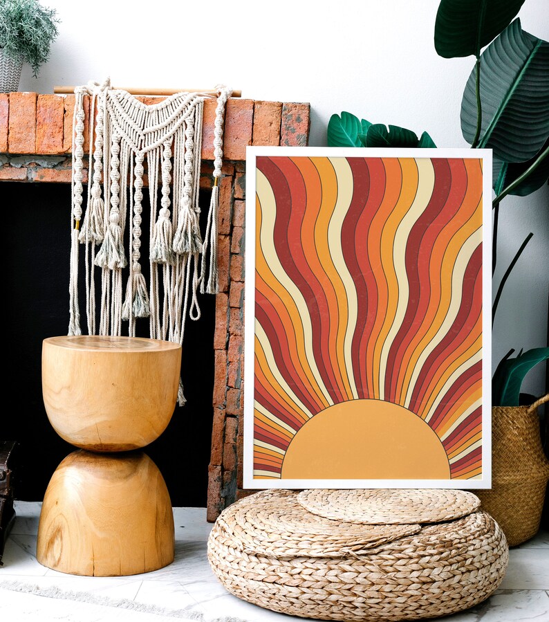 May include: A framed print with a retro sunburst design in shades of orange, red, and yellow. The print is hanging on a brick wall above a wooden stool.