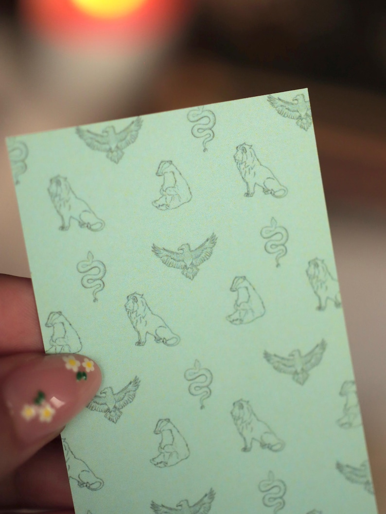 Puede incluir: Una tarjeta rectangular de color verde claro con un patr&oacute;n repetitivo de ilustraciones de l&iacute;neas verde oscuro. El dise&ntilde;o incluye representaciones de &aacute;guilas con las alas extendidas, serpientes enroscadas, leones sentados y tejones en cuadr&iacute;cula.
