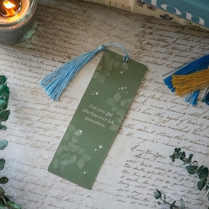 Puede incluir: Marcap&aacute;ginas verde con un borla azul. El marcap&aacute;ginas tiene un fondo blanco con hojas verdes y purpurina plateada. El texto en el marcap&aacute;ginas dice "Para cada chica que alguna vez se ha sentido impotente."