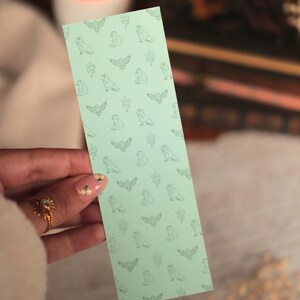 Puede incluir: Un marcap&aacute;ginas rectangular de color verde menta claro con un patr&oacute;n repetitivo de peque&ntilde;as ilustraciones de l&iacute;neas en verde oscuro de varios animales, incluyendo p&aacute;jaros, serpientes y mam&iacute;feros sentados, dispuestos en una cuadr&iacute;cula.