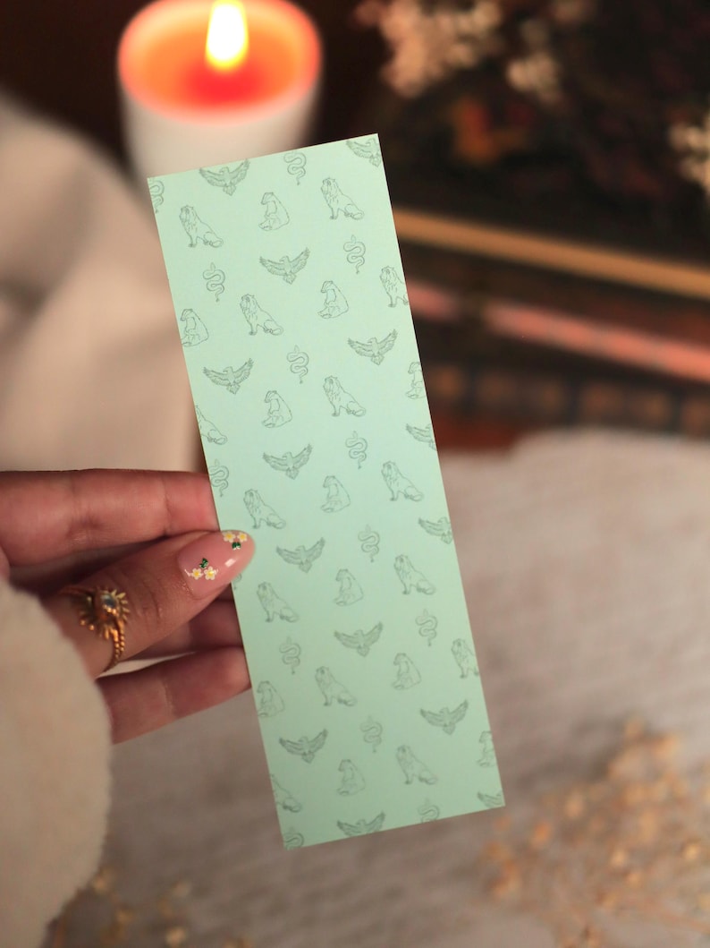 Puede incluir: Un marcap&aacute;ginas rectangular de color verde menta claro con un patr&oacute;n repetitivo de peque&ntilde;as ilustraciones de l&iacute;neas en verde oscuro de varios animales, incluyendo p&aacute;jaros, serpientes y mam&iacute;feros sentados, dispuestos en una cuadr&iacute;cula.