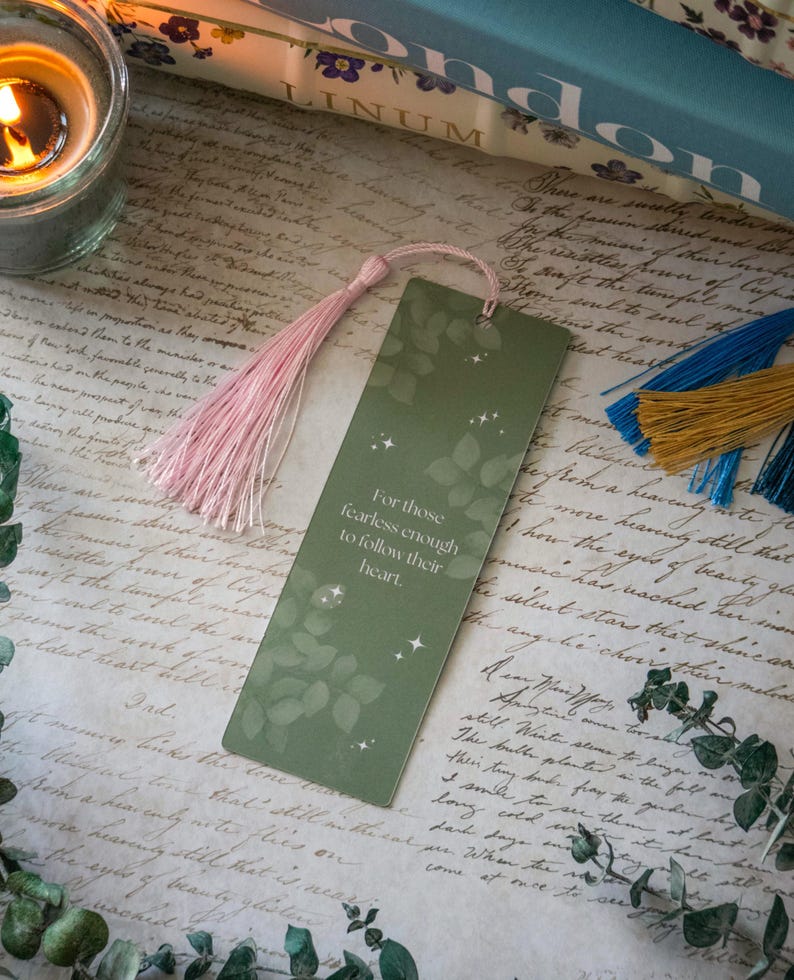 Puede incluir: Un marcap&aacute;ginas verde con un borla rosa. El marcap&aacute;ginas tiene un dise&ntilde;o de hojas y el texto "Para aquellos que son lo suficientemente valientes para seguir su coraz&oacute;n."