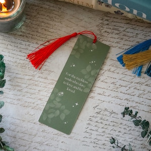 Puede incluir: Un marcap&aacute;ginas verde con un dise&ntilde;o de hojas y estrellas doradas. El marcap&aacute;ginas tiene un borla roja y el texto "Para las almas imprudentes que se atreven a amar y ser amadas."
