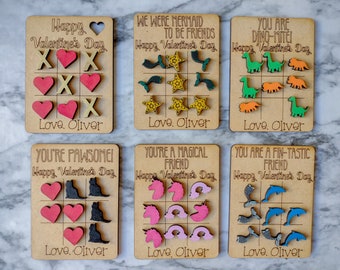 May include: Six wooden Valentine's Day cards with different themes. Each card has a tic-tac-toe board with different images to play with. The cards say "Happy Valentine's Day" and "Love, Oliver".