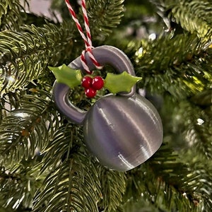 May include: A silver-coloured Christmas ornament shaped like a kettlebell with a sprig of holly and red berries.
