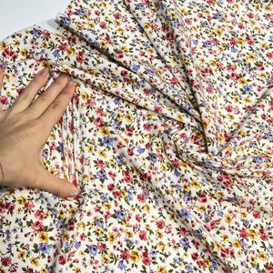 May include: White fabric with a small floral print in shades of pink, blue, yellow, and green.