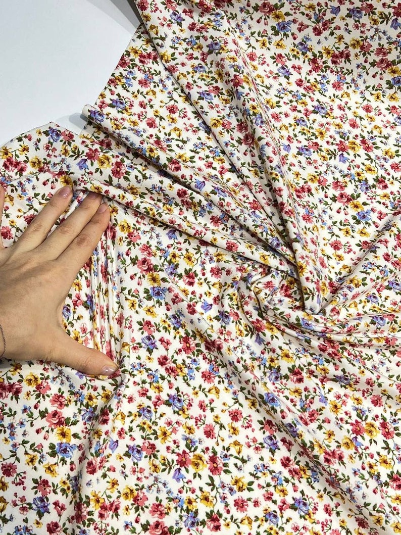 May include: White fabric with a small floral print in shades of pink, blue, yellow, and green.