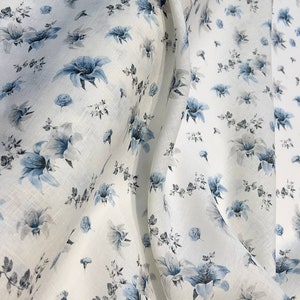 May include: White linen fabric with a blue floral pattern. The fabric is soft and has a subtle sheen. The flowers are small and delicate, and they are scattered randomly across the fabric.