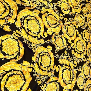 May include: Black fabric with a gold baroque pattern. The pattern features intricate floral designs and swirling lines.
