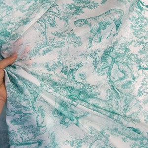 May include: White fabric with a teal green toile pattern featuring tigers, trees, and foliage. The fabric is draped, showing the detailed illustration of a jungle scene. The design is repeated across the material.