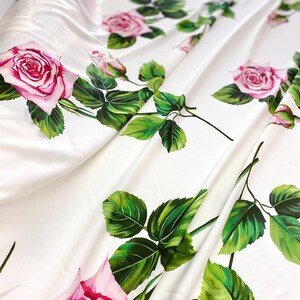 May include: White fabric with a repeating pattern of pink roses and green leaves.