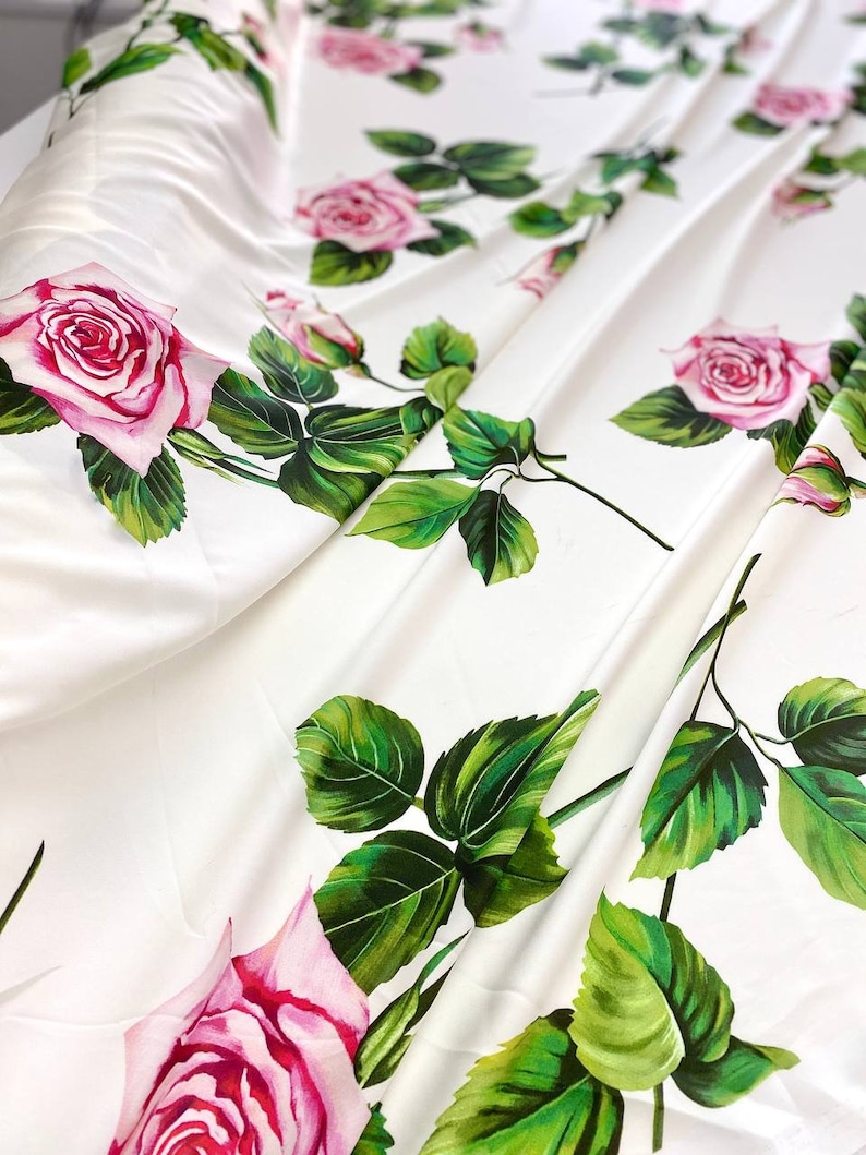 May include: White fabric with a repeating pattern of pink roses and green leaves.
