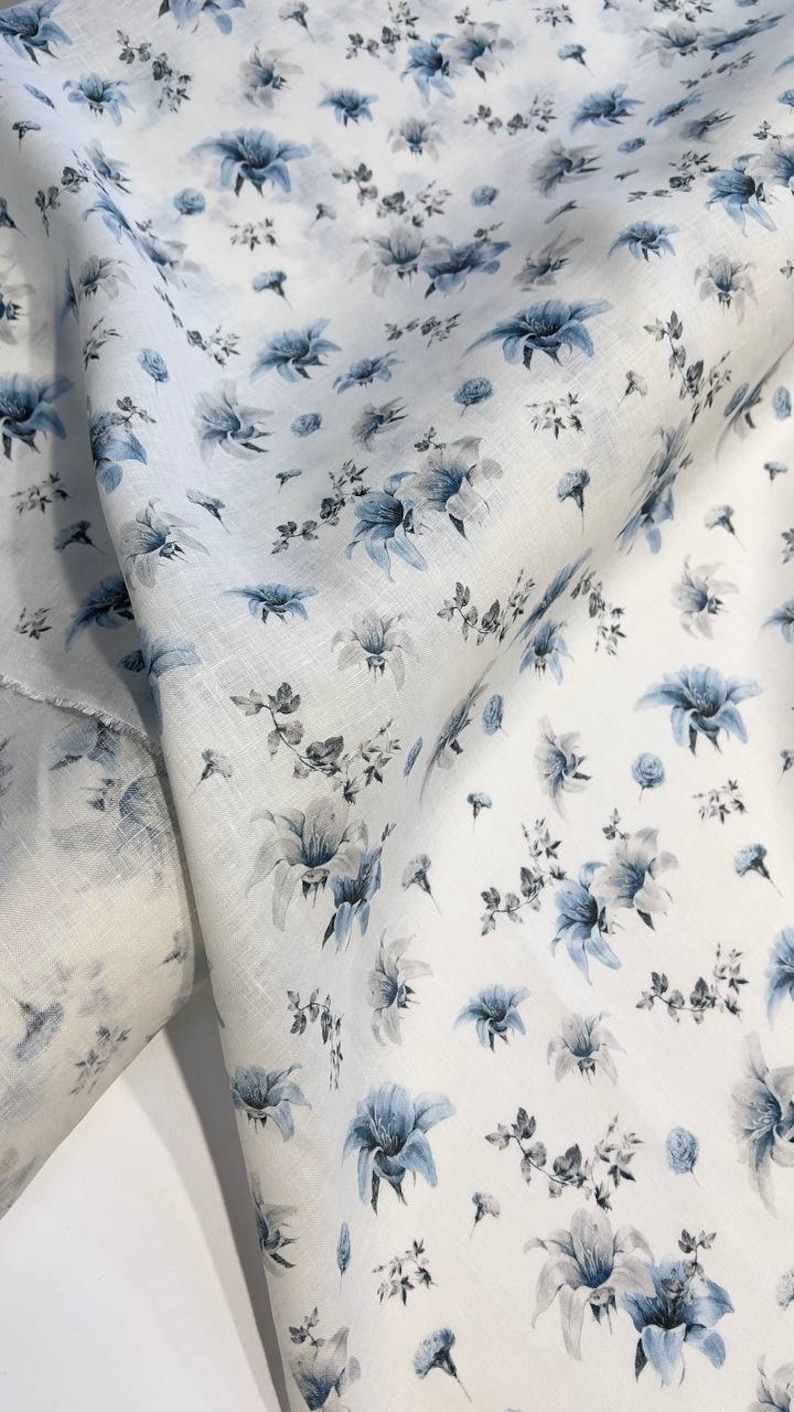 May include: White fabric with a blue floral pattern. The fabric is folded in half and the pattern is visible on both sides.