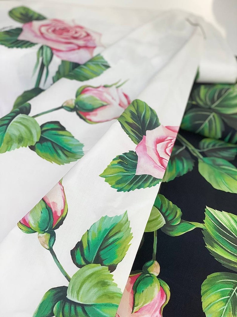 May include: Two fabric swatches with a floral pattern. One swatch is white with pink roses and green leaves. The other swatch is black with pink roses and green leaves.