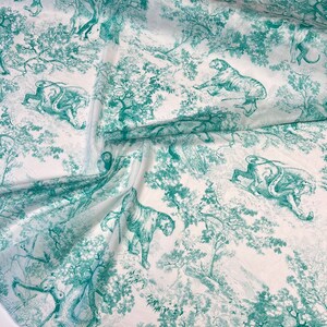 May include: White fabric with a teal green toile pattern featuring tigers, trees, and foliage. The design is a detailed illustration, creating a jungle scene. The fabric is likely used for apparel or home decor.