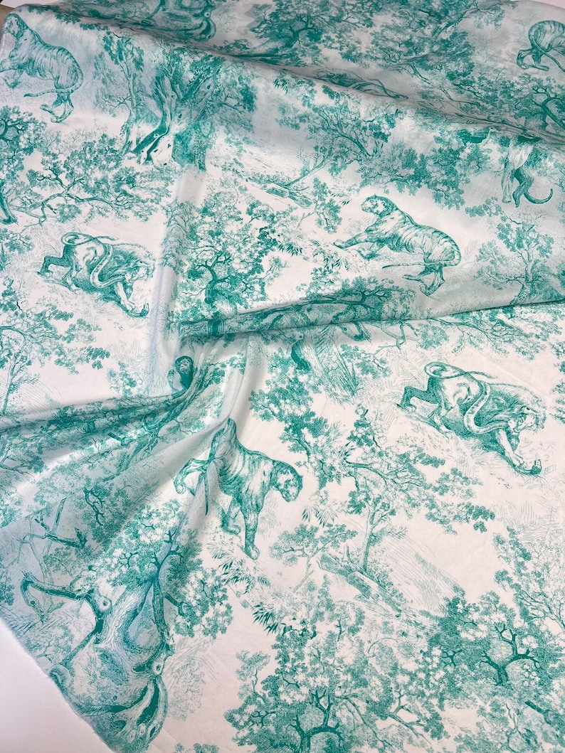 May include: White fabric with a teal green toile pattern featuring tigers, trees, and foliage. The design is a detailed illustration, creating a jungle scene. The fabric is likely used for apparel or home decor.