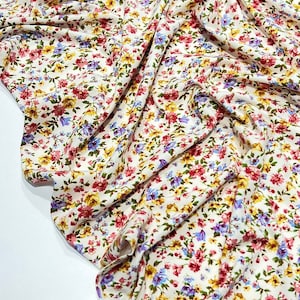 May include: White fabric with a small floral print in shades of pink, yellow, and blue.