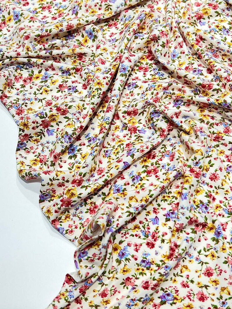 May include: White fabric with a small floral print in shades of pink, yellow, and blue.