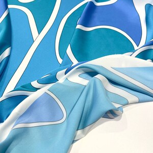 May include: A blue and white patterned fabric with a flowing, draped design. The fabric features abstract shapes and lines in shades of blue and white.
