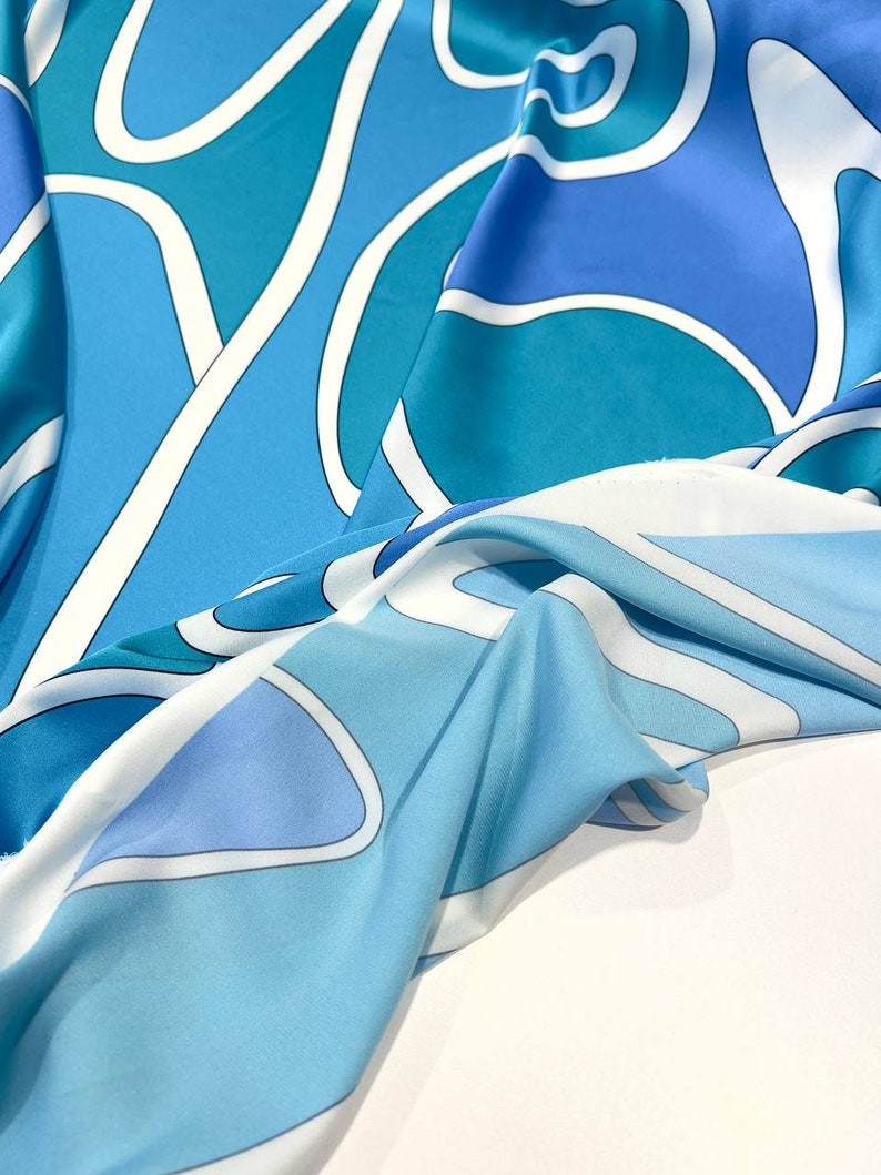 May include: A blue and white patterned fabric with a flowing, draped design. The fabric features abstract shapes and lines in shades of blue and white.