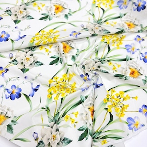 May include: White fabric with a floral print featuring yellow, blue, and white flowers. The fabric has a satin-like sheen.