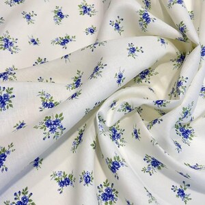 Pu&ograve; includere: Tessuto bianco con un piccolo motivo floreale blu. Il tessuto &egrave; piegato e drappeggiato.
