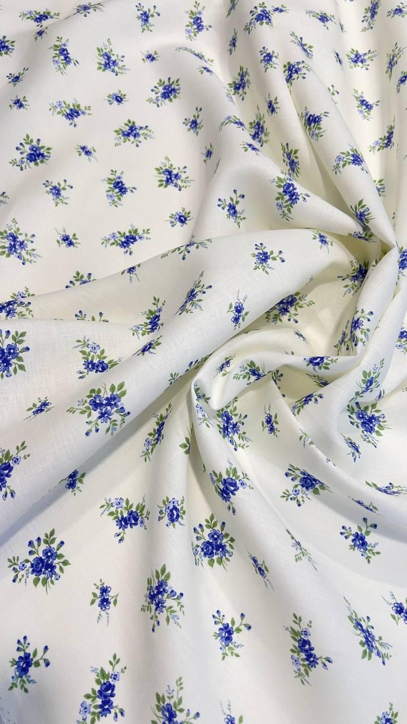 Pu&ograve; includere: Tessuto bianco con un piccolo motivo floreale blu. Il tessuto &egrave; piegato e drappeggiato.